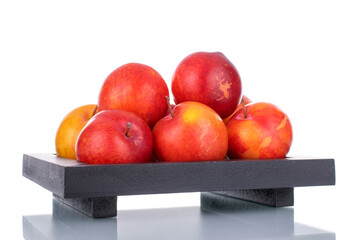 Several juicy organic yellow-red plums on a wooden tray, close-up, isolated on white.