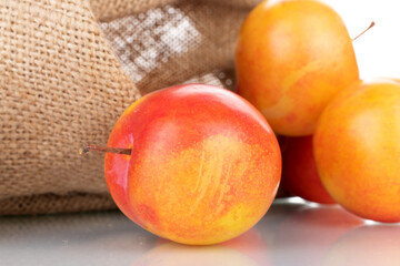 Several juicy organic yellow-red plums with a jute bag, close-up, isolated on white.