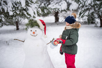 Happy blonde cute child girl plaing with a snowman