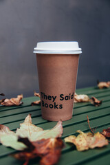 a paper cup with coffee stands on a street table surrounded by autumn leaves