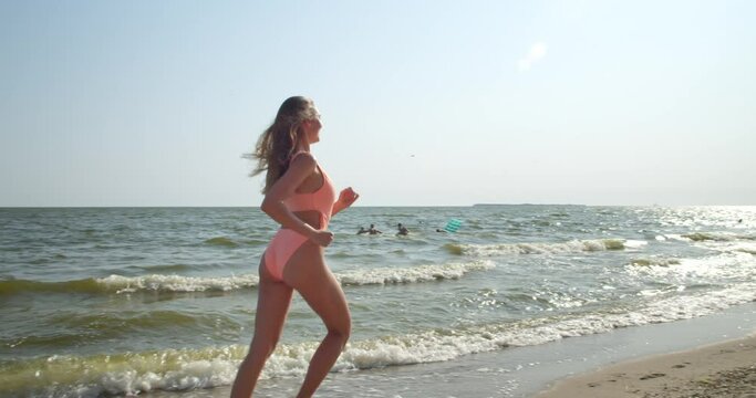 Beautiful young woman in swimming suit running on sea beach