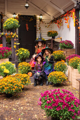 Happy Halloween! Three cute little laughing girls in witches costumes are coming to the house for sweets.