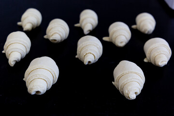 Lots of raw croissants on a black baking sheet.