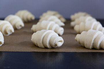 Fototapeta na wymiar Raw shaped and rolled-in croissants lie in rows on the baking sheet. The handmade croissant preparation process