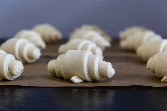 Raw shaped and rolled-in croissants lie in rows on the baking sheet. The handmade croissant preparation process
