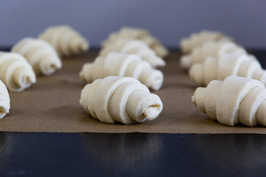 Raw shaped and rolled-in croissants lie in rows on the baking sheet. The handmade croissant preparation process