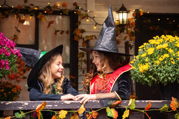 Happy Halloween! Two cute little laughing girls in witches costumes are coming to the house for sweets.

