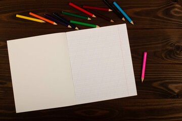 School notebook with oblique lines, colored pencils on the table wooden background. Blank sheet of...