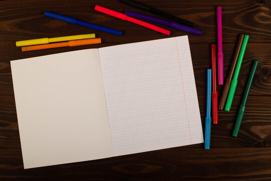 School notebook with oblique lines, colored felt-tip pen on the table wooden background. Blank sheet of paper in notebook on the desk. Back to school. School supplies. Top view. Copy space for text