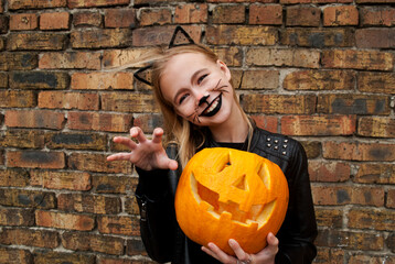 Beautiful teenager girl dressed as a black cat for Halloween. Child holding a pumpkin monster for Halloween. 
