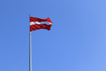 Fototapeta premium Latvian national flag on a background of blue sky