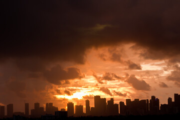 Fototapeta na wymiar front view, very far distance of a silhouette of Miami skyline at dawn with clouds providing golden sky, with powerful light 