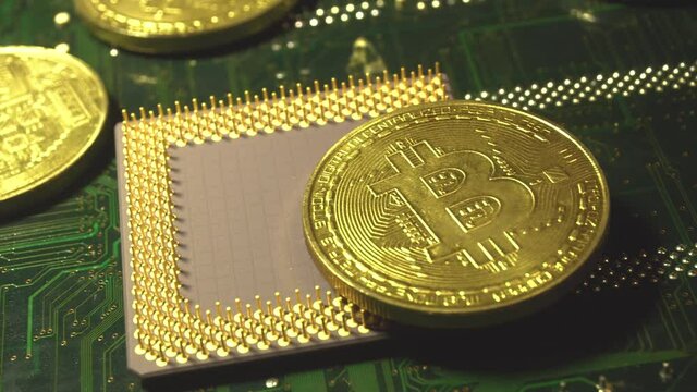 A gold Bitcoin coin with glare and reflection installed instead of a central processor in the motherboard with electronic components with light and smoke in the darkness. Bitcoin Mining