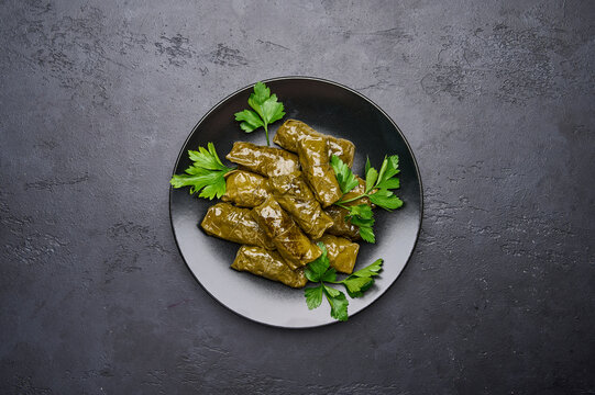Top view delicious stuffed grape leaves dolma with parsley in black plate on dark wood background. Copy space
