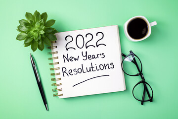 New year 2022 Resolutions on desk. 2022 goals with open notebook, coffee cup, eyeglasses, succulent...