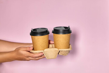 Close-up on a pink background, a woman's hand holds a paper cup with coffee in a stand. Coffee or tea to go. People hands passing one another cup of coffee, coffee delivery.