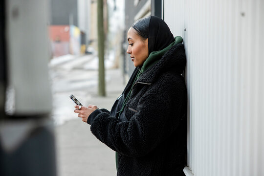 Young woman in headscarf using smart phone on city sidewalk