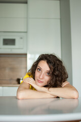Beautiful curly girl in yellow t-shirt is looking at the camera at home in her apartment, posing with smile, happy people concept