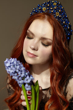 A red-haired woman with her eyes closed. Holds a blue hyacinth flower. On the head of the diadem is blue. High quality photo
