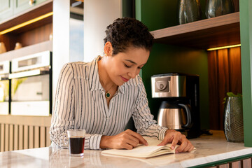 happy woman reading book and drinking coffee in kitchen counter