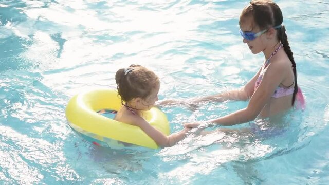 Two young smiling girls in a swimsuit bathes play in a pool with blue clear water in blue swimming glasses. Summer. Rest. Vacation.
