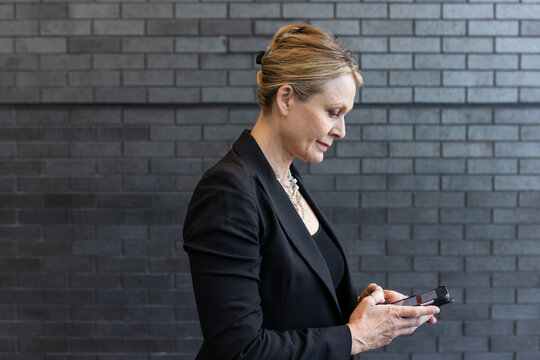 Businesswoman using smart phone at brick wall