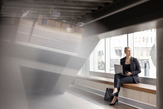 Businesswoman with laptop on office lobby bench