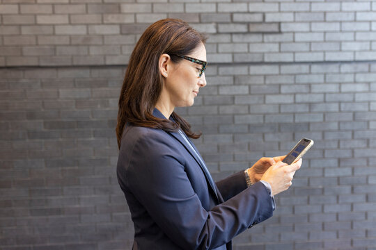 Businesswoman in suit using smart phone at brick wall