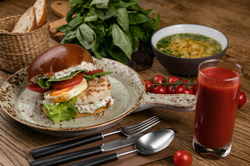 Hamburger with chicken cutlet, soup, tomato juice, basil, tomatoes on the table.
