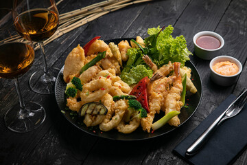 assorted grilled seafood with sauce and white wine on a black table.
