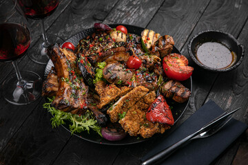 Assorted grilled meat with sauce and red wine on a black table.
