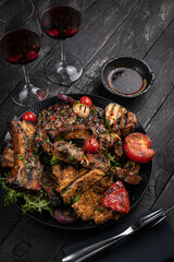 Assorted grilled meat with sauce and red wine on a black table.
