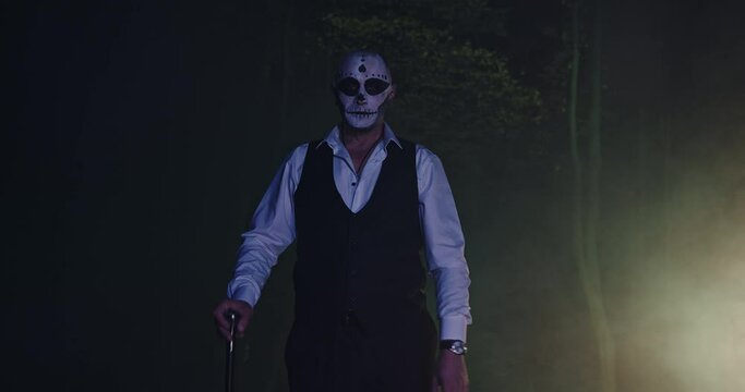 Spooky man with a make-up stick in a dark forest in a dead man's costume for Halloween