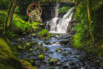 Vintage red waterwheel with waterfall at spring in Glenariff Forest Park, County Antrim, Northern Ireland. Long exposure and soft focus photography