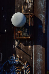 antique white porcelain doorknob and metal keyhole lock on rustic wood door with metal scrollwork...