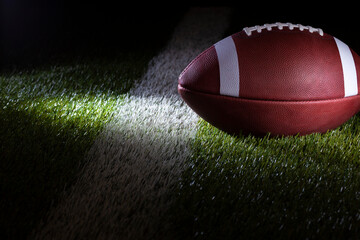 Low angle selective focus view of a football at a yard line with dramatic lighting