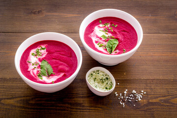 Two white bowls of red beet soup with sour cream and green herbal salt