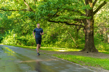 Fototapeta premium A man athlete runs in the park outdoors, around the forest, oak trees green grass young enduring athletic athlete active runner forest, fitness trail young legs motion, woods outside. Summer energy