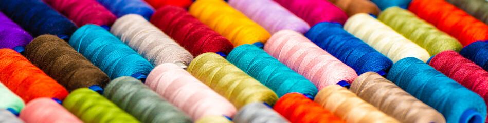 Multi-colored sewing threads laid out in a row. Bright background. - obrazy, fototapety, plakaty