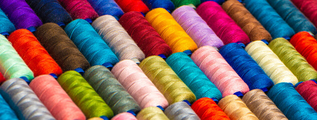 Multi-colored sewing threads laid out in a row. Bright background.