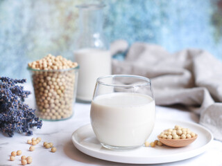 A glass of soy milk in a white plate with its beans in background, plant-based milk is an...
