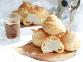 French choux dough pastry cream puff, filled with white sweet cream with a cup of coffee on table 