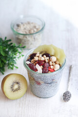 A cup of overnight chia seed almond milk pudding with dried berries fruit and kiwi,  healthy nuts on wooden table. Chia pudding is high in protein, full of omega-3s, packed with fiber