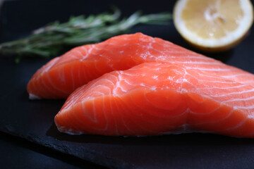 Close up of sliced piece of raw fresh salmon with rosemary and lemon on a black plate, it's having a lot of nutrition's value and good for health 