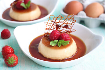 Plate of cream caramel custard with spun sugar decoration, strawberries and raspberries. With eggs in background. It is a custard dessert with a layer of clear caramel sauce
