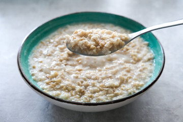 A spoon of cooked oats porridge above a green bowl, healthy breakfast and dieting product close up, tasty vegan food