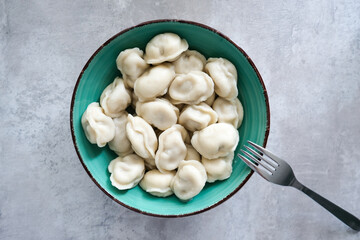 Tasty meat dumplings in green plate with fork on a table, russian pelmeni