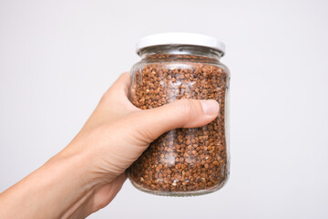 Hand holding a pot of buckwheat agaonst white background, national russian food symbol of crisis and economy, food supplies