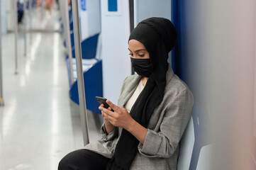 Muslim adult woman sitting on subway while using her cellphone