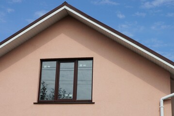 facade of a house with a pink wall and a one brown window against the blue sky